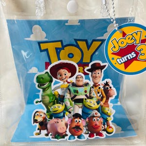 May include: A clear plastic bag featuring characters from the animated film "Toy Story." The bag has a blue background with the word "Toy" in yellow. A circular tag reads "Joey turns 3."