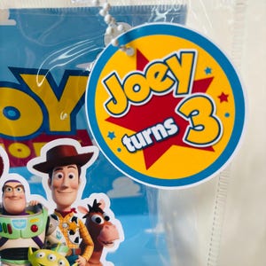 May include: A white ceramic mug with a black handle and the text "But First, Coffee" in a bold, black font. The mug is set against a blurred background, suggesting a cozy setting.