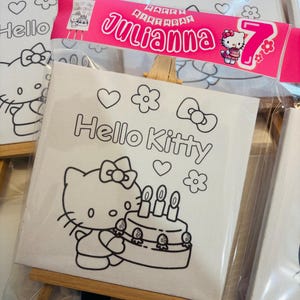 May include: White canvas art featuring a Hello Kitty design, packaged in clear plastic. The design includes Hello Kitty with a birthday cake, hearts, and flowers. A pink banner reads "Happy Birthday Julianna 7".