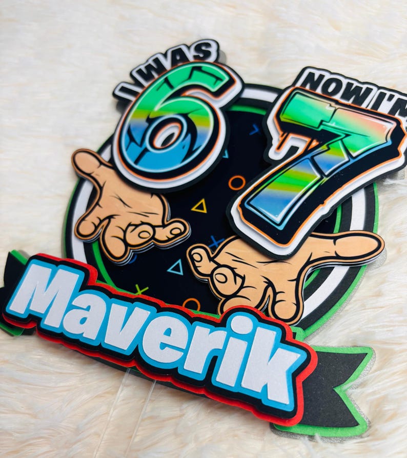May include: A layered birthday cake topper with the text "I WAS 6 NOW I'M 7" in a graffiti style. The name "Maverik" is also displayed. The design includes hands, geometric shapes, and a black, green, and white color scheme.