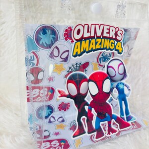 May include: Clear plastic tote bag with a white insert featuring Spider-Man characters and the text "OLIVER'S AMAZING 4". The bag has clear handles and a white snap closure. Colorful stickers of Spider-Man characters are also visible.