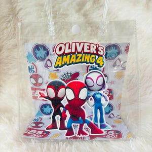 May include: Clear plastic gift bag with a handle, featuring the text "OLIVER'S AMAZING 4" and illustrations of Spider-Man characters. The bag has a white background with various Spider-Man-themed icons and the words "EBS - GO!"