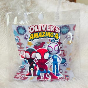 May include: Clear plastic gift bag with a white paper insert featuring the text "Oliver's Amazing 4" and cartoon images of Spider-Man characters. The bag has clear plastic handles and a white button closure.