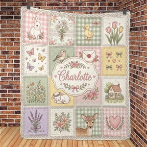 May include: A quilted blanket featuring a grid of illustrations including a rabbit, daisies, a duckling, tulips, butterflies, a bird, an envelope, bows, hearts, wildflowers, a lamb, a house, lavender, and a deer, with the name Charlotte in the centre.