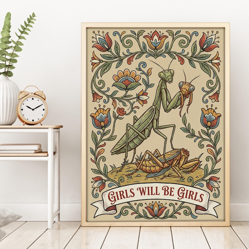 May include: A framed art print featuring a green praying mantis holding a smaller insect, with the text "GIRLS WILL BE GIRLS" on a banner. The artwork has a floral border with red, blue, and orange accents.