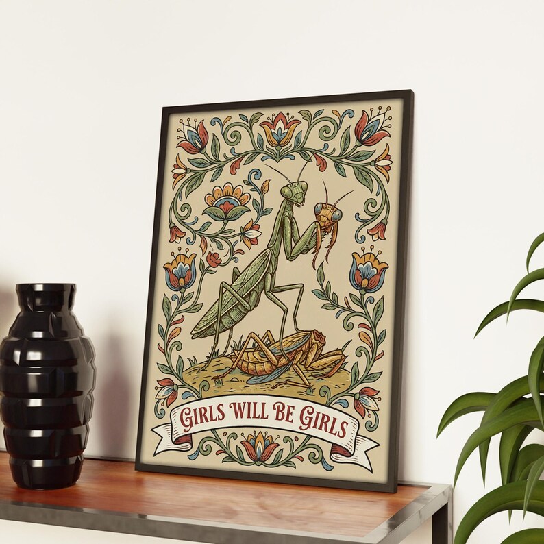May include: Framed art print featuring a detailed illustration of two praying mantises, one holding a smaller insect. The artwork is surrounded by a floral border with a banner that reads "GIRLS WILL BE GIRLS". The color palette includes green, beige, red, and blue.