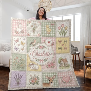 May include: A quilted blanket featuring a grid of pastel-coloured squares with illustrations of a rabbit, flowers, a duckling, tulips, butterflies, a bird, an envelope, bows, a lamb, a house, lavender, and a deer, with the name Charlotte in the centre.
