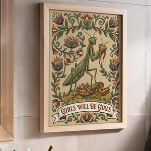 May include: Framed art print featuring a green praying mantis holding a smaller insect, with a second insect below. The artwork is surrounded by floral designs in red, blue, and green, with the text "GIRLS WILL BE GIRLS" on a banner.