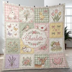 May include: A pastel-colored quilt featuring a patchwork design with various illustrations. The quilt includes images of a bunny, flowers, a duckling, butterflies, a bird, a lamb, a deer, and a house. The name "Charlotte" is displayed in the center.
