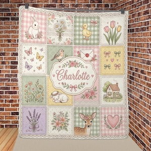 May include: A patchwork quilt featuring a central oval label with the name Charlotte, surrounded by squares depicting a rabbit, a duckling, a deer, a house, flowers, butterflies, bows, a heart, and an envelope, all in soft pastel colours.