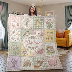 May include: A quilted blanket featuring a patchwork design with pastel-coloured squares displaying illustrations of a rabbit, flowers, a duckling, butterflies, a bird, an envelope, bows, a lamb, a house, lavender, and a deer, with the name Charlotte.