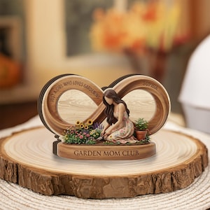 Puede incluir: Signo de infinito de madera con una figura de jardinero, girasoles y el texto "Just a girl who loves gardening" y "Garden Mom Club". La figura está arrodillada, cuidando un macizo de flores. También es visible el nombre "Sophia".