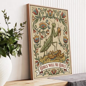 May include: A framed art print featuring a green praying mantis with a smaller insect, surrounded by floral elements in red, blue, and orange. The text "GIRLS WILL BE GIRLS" is displayed on a banner at the bottom.