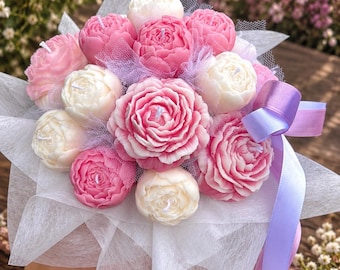 May include: A bouquet of peony-shaped candles in shades of pink and white, each featuring a central wick. The candles are arranged together, wrapped in white translucent paper and light purple tulle, and tied with a light purple satin ribbon.