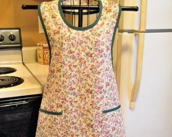 May include: A floral print apron with green trim and two pockets. The apron is made of a lightweight fabric and has a simple design.