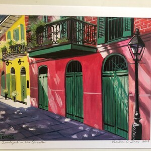 May include: A painting of a narrow street in New Orleans with colorful buildings and green doors. The buildings have balconies and are painted in shades of yellow, pink, and red. The street is paved with gray stones and there is a lamppost on the right side of the image. The painting is signed "K. Jones 2019" and titled "Sunlight in the Quarter".