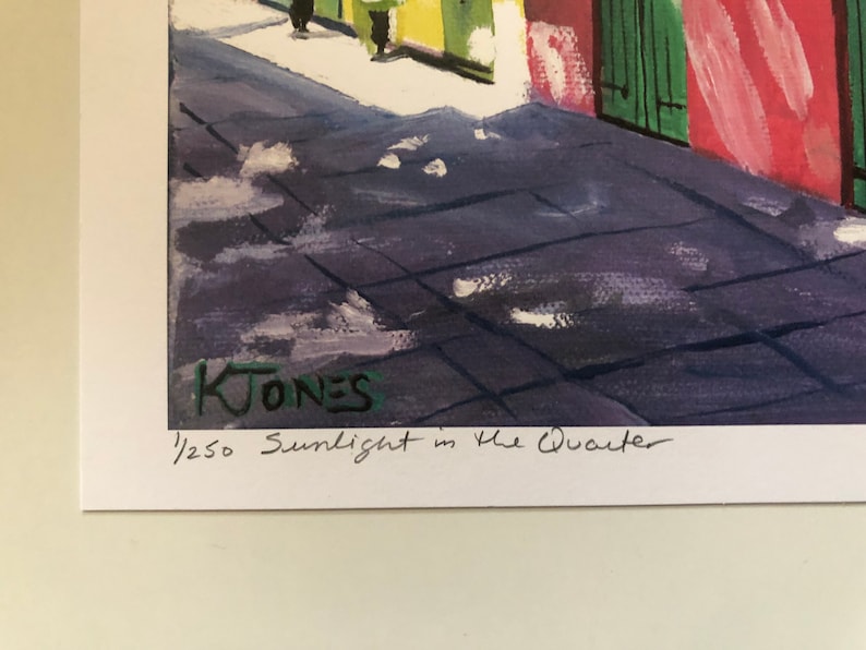 May include: A watercolor painting of a street scene in the French Quarter of New Orleans. The painting is signed "K. Jones" and numbered "1/250" in the lower right corner. The title of the painting is "Sunlight in the Quarter".
