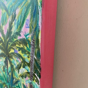 May include: Close-up of the edge of a painting depicting a tropical scene with palm trees and lush foliage. The painting is framed with a pink wood frame.