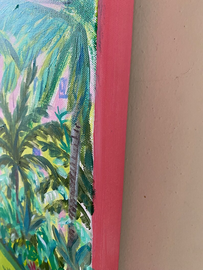 May include: Close-up of the edge of a painting depicting a tropical scene with palm trees and lush foliage. The painting is framed with a pink wood frame.