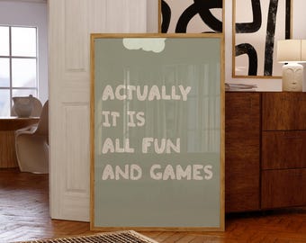 May include: A framed poster with the text "ACTUALLY IT IS ALL FUN AND GAMES" in white letters on a sage green background. The poster is leaning against a wall in a room with wooden floors and other framed art.