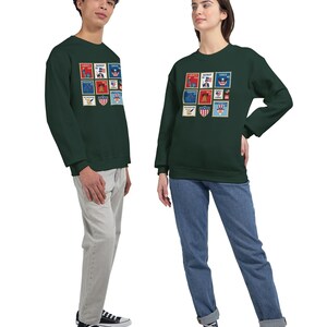 May include: Two people wearing matching dark green sweatshirts. The sweatshirts display a grid of colourful postage stamp designs with patriotic themes. The stamps include images of eagles, flags, and other symbols. One person wears light grey trousers, the other blue jeans.