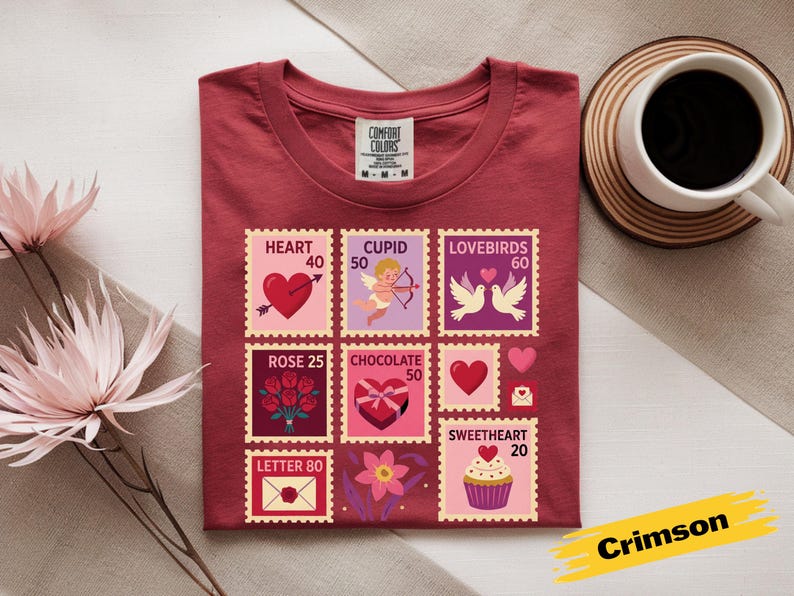 Op de afbeelding: Karmizijnrood T-shirt met Valentijnsdag postzegelontwerpen. De postzegels tonen harten, Cupido, tortelduifjes, rozen, chocolade en een cupcake. Het shirt bevat de tekst "Comfort Colors" en de kleurnaam "Crimson".