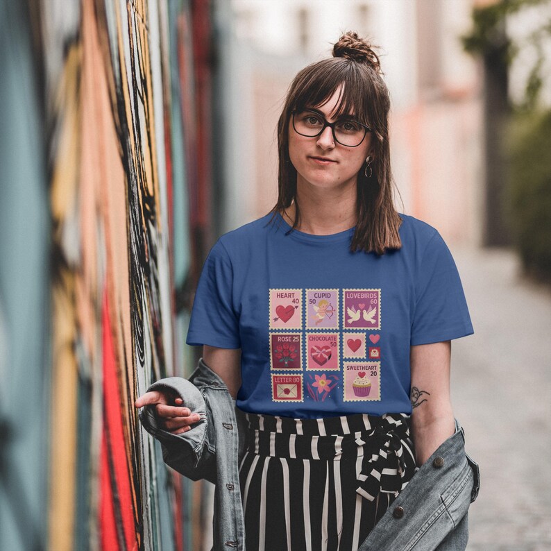 Op de afbeelding: Een blauw t-shirt met een reeks postzegelontwerpen met Valentijnsdagthema. De postzegels tonen harten, Cupido, tortelduifjes, rozen, chocolade en cupcakes. Het t-shirt wordt gedragen door een persoon met een bril.