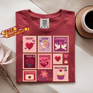 Op de afbeelding: Een bordeauxrood t-shirt met een postzegelachtig ontwerp met harten, Cupido, rozen en tortelduiven. Het ontwerp bevat de tekst "HEART 40", "CUPID 50", "LOVEBIRDS 60", "ROSE 25", "CHOCOLATE 50", "SWEETHEART 20" en "LETTER 80".