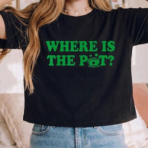 May include: Black t-shirt with the green text "WHERE IS THE POT?" and a green shamrock graphic. The shirt is paired with blue jeans. A casual, everyday wear tee.