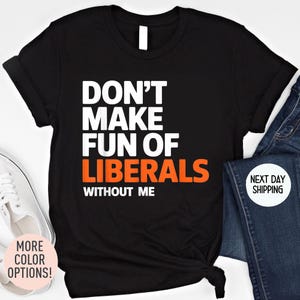 May include: Black t-shirt with the text "DON'T MAKE FUN OF LIBERALS WITHOUT ME" in white and orange. The shirt is displayed with a pair of blue jeans and white sneakers.