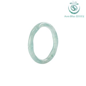 May include: A light green jade bangle bracelet. The bracelet has a smooth, polished surface and a slightly irregular shape. The Aura Bliss logo is in the upper right corner.