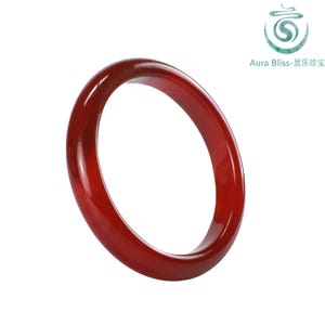 Pode incluir: Uma pulseira de bracelete vermelha escura e polida. O design liso e circular é feito de um material translúcido que reflete a luz. A pulseira é de cor sólida com um acabamento brilhante. A imagem inclui o texto "Aura Bliss-灵乐珍宝".