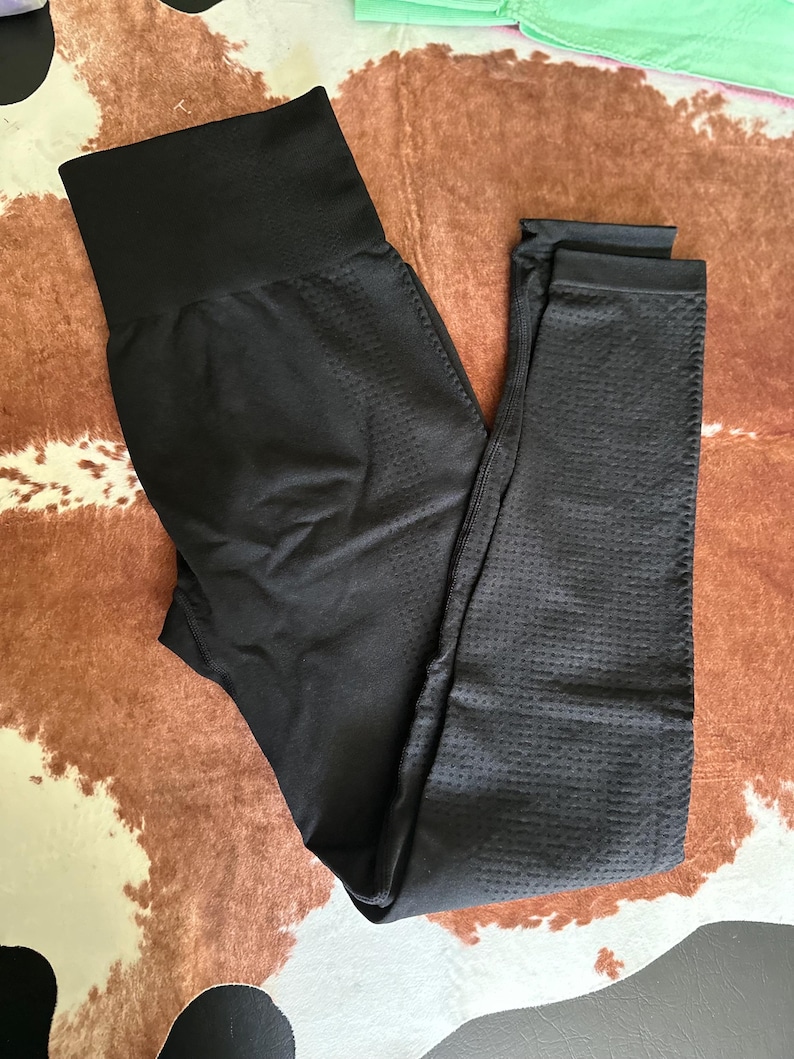 May include: Black leggings with a high waistband. The leggings have a textured, perforated pattern on the legs and a smooth, solid waistband. The leggings are made of a stretchy material and are designed for athletic activities.