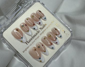 May include: A set of handmade press-on nails in a clear plastic case. The nails have a nude base with a white French tip and are adorned with small, colorful gemstones. The text "Handmade Nails" and "Brighten up your finger, Brighten up your life!" is printed on the packaging.