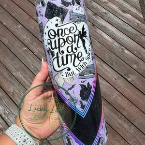 May include: A purple and black tumbler with a glitter finish. The tumbler features a graphic of books, typewriters, and bats. The text "Once upon a time, but with spice" is printed on the tumbler.