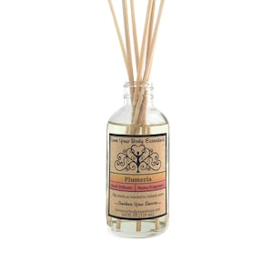 May include: A clear glass reed diffuser bottle filled with a light yellow liquid and wooden reeds. The label reads "Plumeria" and "Reed Diffuser Home Fragrance". The bottle contains 4.0 FL OZ (118 mL) of liquid.