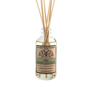 May include: A clear glass bottle with a brown label that reads "Love Your Body Essentials Pine Reed Diffuser Home Fragrance Pip reeds as needed to refresh scent...Awaken Your Senses...loveyourbodvessentials.com 4.0 FL OZ (118 ml)". The bottle is filled with a clear liquid and has wooden sticks inserted into it.