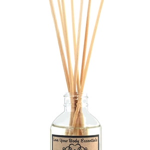 Puede incluir: Una botella de vidrio con una etiqueta marr&oacute;n que dice "Love Your Body Essentials" y "Orange Vanilla Reed Diffuser Home Fragrance". La etiqueta tambi&eacute;n incluye el texto "Flip reeds as needed to refresh scent...Awaken Your Senses...loveyoubodyessentials.com 4.0 FL OZ (118 mL)". La botella est&aacute; llena de un l&iacute;quido transparente y tiene palitos de madera insertados en ella.