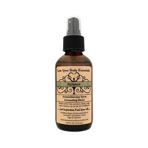 May include: A brown glass bottle with a black spray top. The label is beige with green text and a green tree design. The text on the label reads "Love Your Body Essentials", "Balance", "Aromatherapy Spray", "Grounding Blend", "Shake well. Use on face, body, yoga mats, linens, or as an air freshener", "Let Inspiration Fuel Your Life", "Distilled Water & Essential Oils of Lavender, Geranium, Clary Sage & Cypress", "www.loveyourbodyessentials.com", "4.0 FL OZ (118 ml.)".