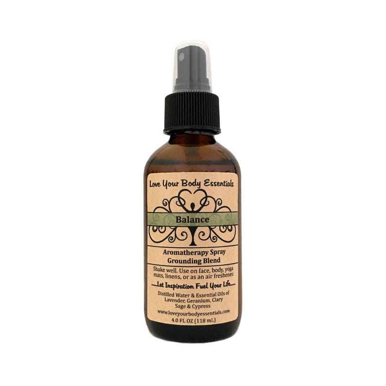 May include: A brown glass bottle with a black spray top. The label is beige with green text and a green tree design. The text on the label reads "Love Your Body Essentials", "Balance", "Aromatherapy Spray", "Grounding Blend", "Shake well. Use on face, body, yoga mats, linens, or as an air freshener", "Let Inspiration Fuel Your Life", "Distilled Water & Essential Oils of Lavender, Geranium, Clary Sage & Cypress", "www.loveyourbodyessentials.com", "4.0 FL OZ (118 ml.)".