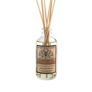 May include: A clear glass bottle with a brown label that reads "Love Your Body Essentials" and "Brown Sugar Fig Reed Diffuser | Home Fragrance". The label also includes the text "Flip reeds as needed to refresh scent... Awaken Your Senses... loveyourbodyessentials.com 4.0 FL OZ (118 ml)". The bottle is filled with a clear liquid and has wooden sticks inserted into it.