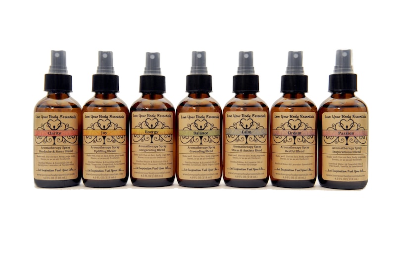 May include: Eight amber glass bottles with spray tops, each labeled with a different aromatherapy blend. The labels feature a stylized tree design and the words "Love Your Body Essentials". The blends are Clarity, Joy, Energy, Balance, Calm, Dream, and Passion.