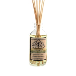 May include: A clear glass bottle with a brown label that reads "Love Your Body Essentials Lemongrass Reed Diffuser Home Fragrance Flip reeds as needed to refresh scent... Awaken Your Senses... loveyourbodyessentials.com 4.0 FL OZ (118 ml.)". The bottle is filled with a light yellow liquid and has wooden sticks inserted into it.