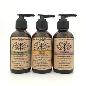 Pode incluir: Tr&ecirc;s garrafas de vidro &acirc;mbar com bombas pretas e etiquetas. Os r&oacute;tulos s&atilde;o marrons com um desenho de &aacute;rvore e o texto "Love Your Body Essentials". As garrafas s&atilde;o etiquetadas como "Rosemary Mint Body Oil", "Citrus Body Oil" e "Lavender Body Oil". Cada garrafa cont&eacute;m 118 ml de &oacute;leo prensado a frio org&acirc;nico.