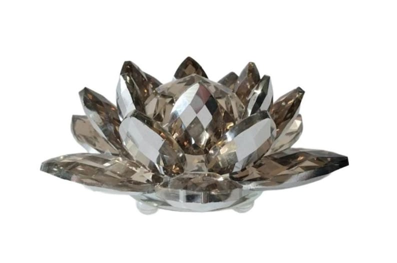 May include: A decorative lotus flower sculpture made of faceted, smoky-colored crystals. The crystal petals are arranged in a circular pattern, with a central, diamond-shaped crystal. The sculpture sits on a clear, round base.