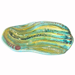 May include: An oval ceramic tray with a wavy, undulating surface. The glaze features a blend of turquoise, teal, and yellow hues, accented by rows of small, raised brown and white dots that follow the curves of the piece.