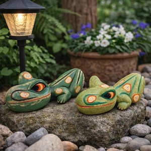 Pode incluir: Quatro estatuetas de sapos verdes com detalhes em laranja e branco são exibidas sobre uma rocha. Os sapos têm olhos detalhados e estão localizados em um jardim com uma lâmpada e plantas em vasos ao fundo. São decorações decorativas para o jardim.