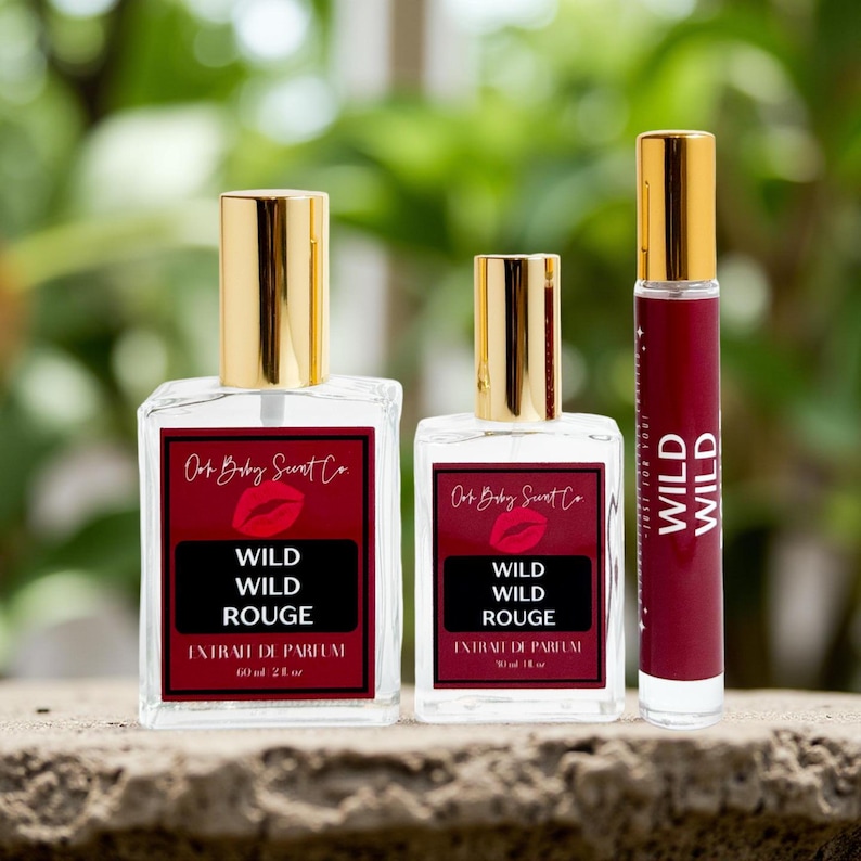 Puede incluir: Tres frascos de perfume con tapas doradas. Dos son cuadrados, etiquetados "Wild Wild Rouge" con un fondo rojo y un gr&aacute;fico de labios. El tercero es un frasco delgado y cil&iacute;ndrico con el mismo texto. Los frascos son transparentes y las etiquetas tienen el texto "extrait de parfum".