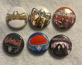 May include: Six round Girlschool band buttons with various designs. The buttons feature the band's logo and images of the band members. Colors include white, red, black, and blue. The buttons are likely made of metal and plastic.