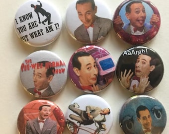 May include: Nine round buttons with different images of Pee-wee Herman. The buttons feature various images of Pee-wee Herman, including him in a suit, on a bicycle, and with his signature catchphrase "I know you are, but what am I?"